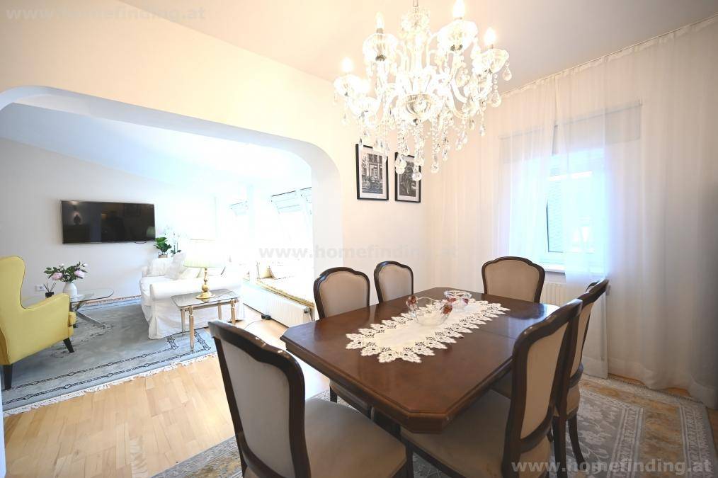 Eleganter Essbereich mit Kronleuchter, Holztisch und Zugang zum hellen Wohnzimmer.