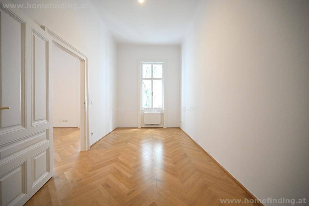 Langer, heller Flur mit Fischgrätparkett und einem Fenster, verbindet verschiedene Räume.