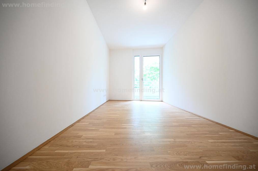 Leeres Zimmer mit Parkettboden und Zugang zu einem französischen Balkon oder einer kleinen Loggia.