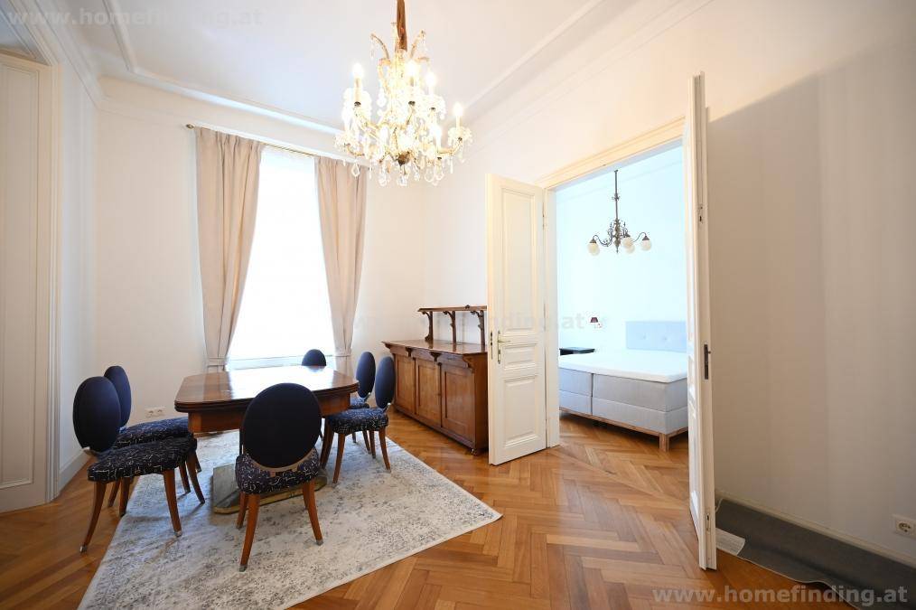Eleganter Essbereich mit Holztisch und Stühlen, der durch eine offene Tür zu einem angrenzenden Schlafzimmer führt.