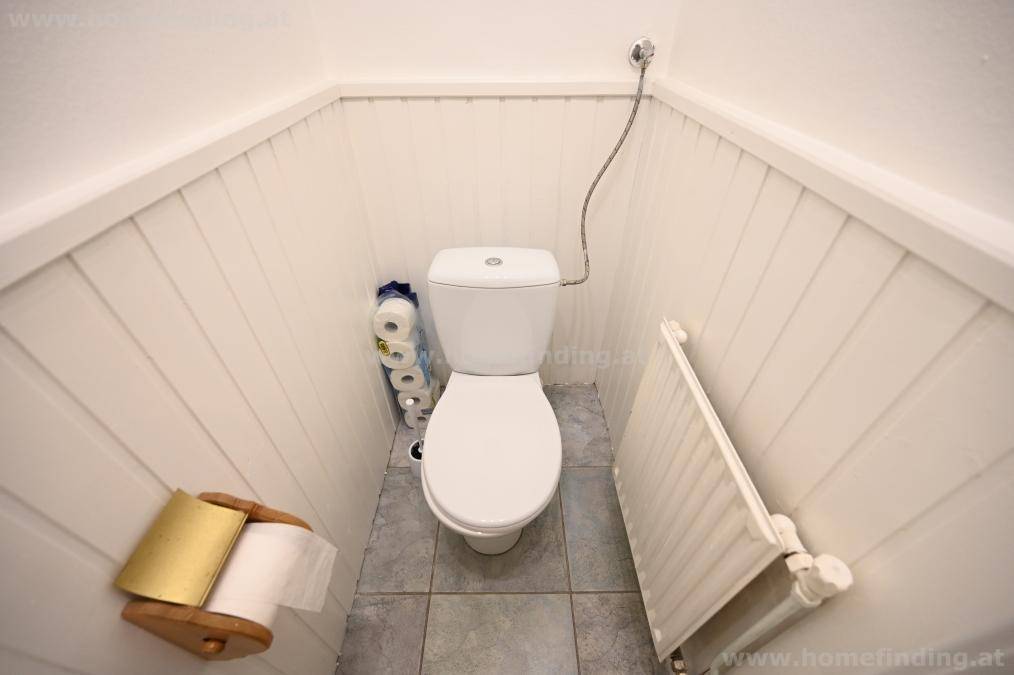 Kleines separates WC mit Toilette, Heizkörper und weißer Holzverkleidung an den Wänden.
