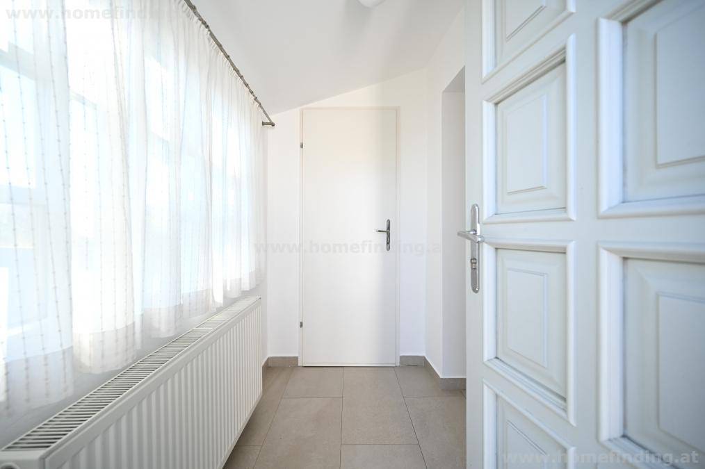 Heller Eingangsbereich mit Fenster, Heizkörper und neutralem Fliesenboden.