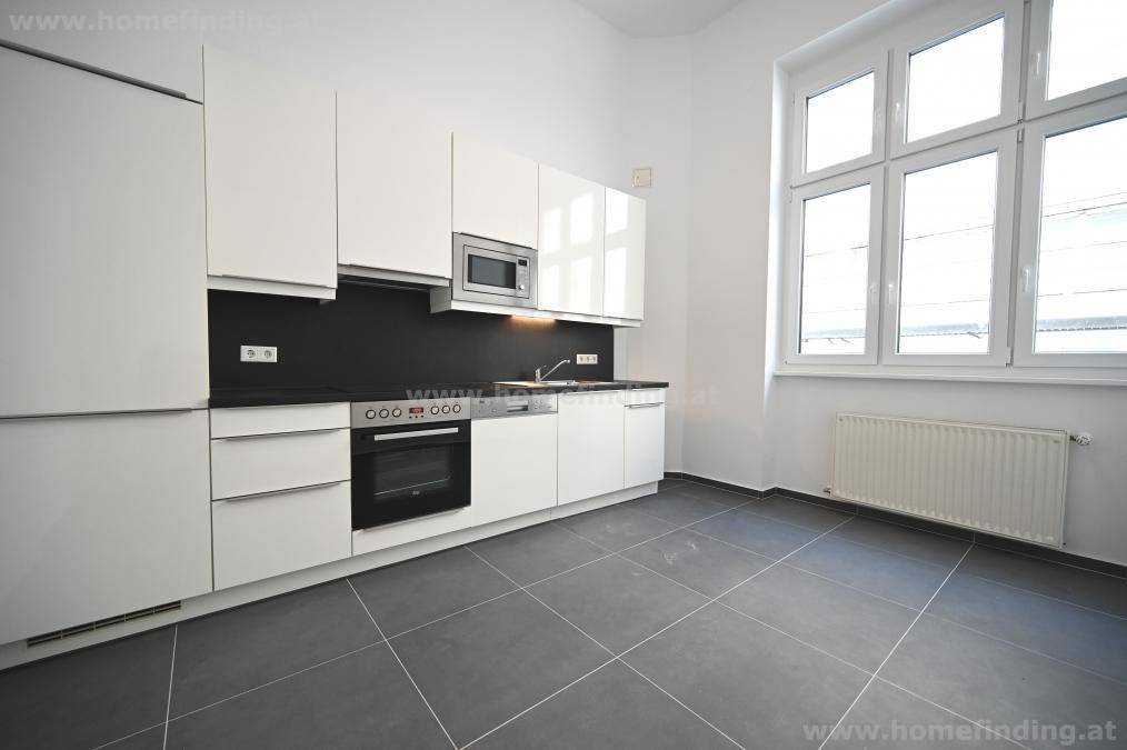 Moderne Küche mit weißen Hochglanzfronten, schwarzer Arbeitsplatte und großem Fenster.