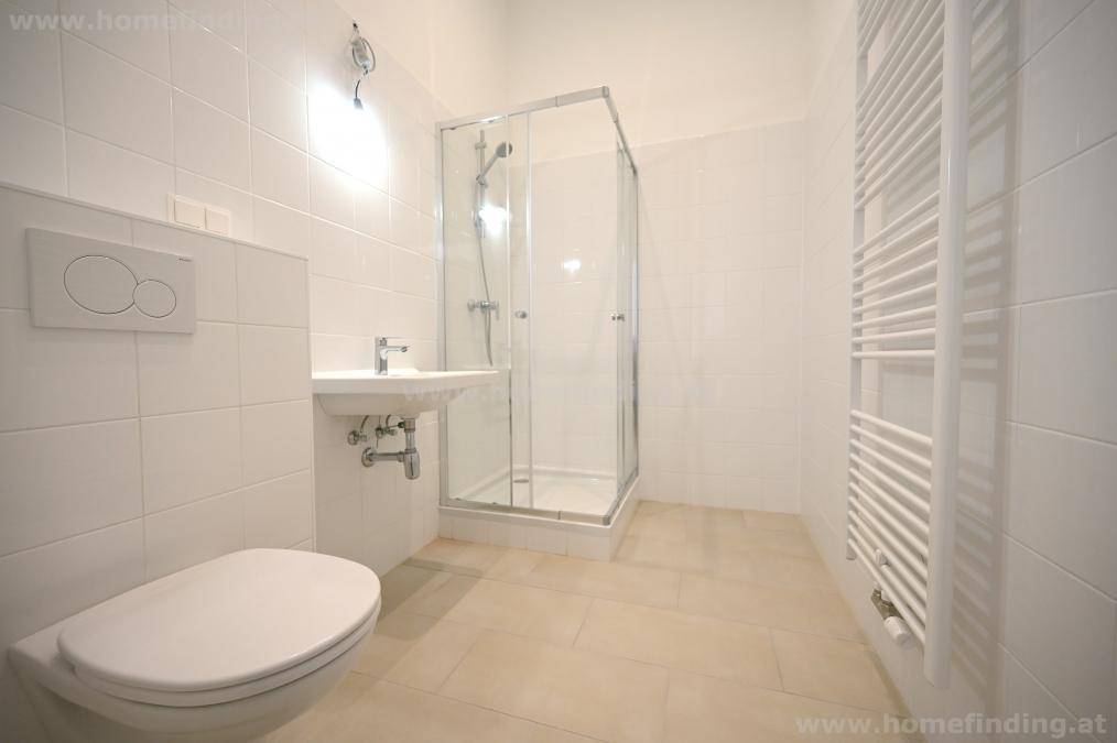 Modernes Badezimmer mit weißen Fliesen, wandhängendem WC, Dusche und beheiztem Handtuchhalter.