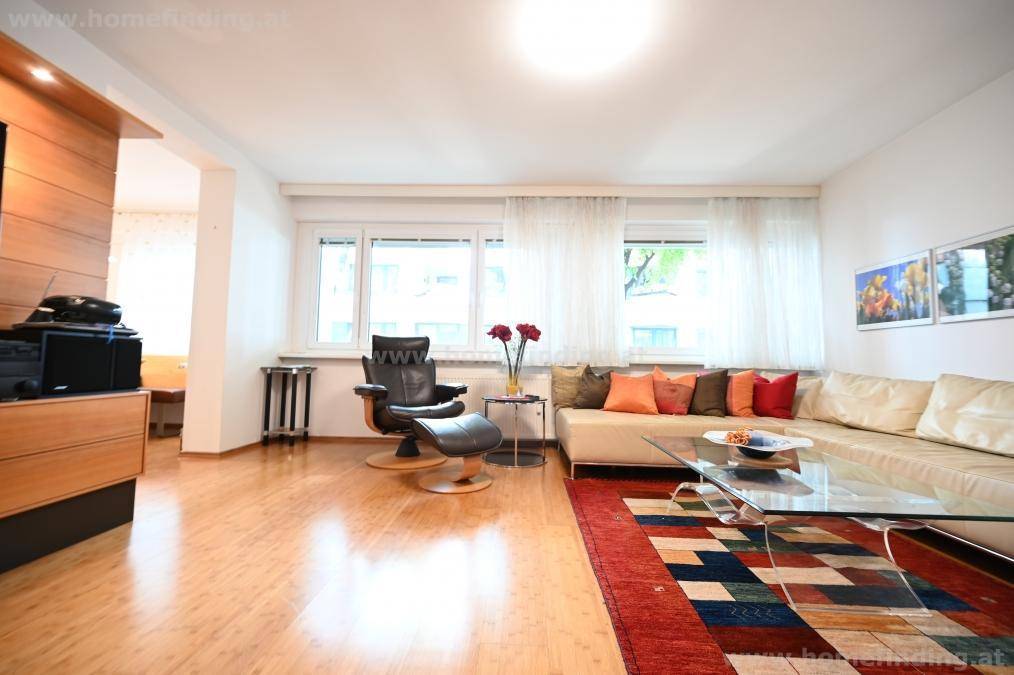 Geräumiges Wohnzimmer mit bequemer Sitzecke, Holzboden und großen Fenstern für viel Tageslicht.
