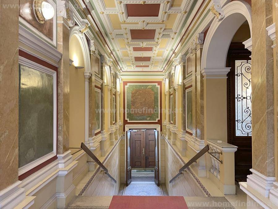Prunkvoller Eingangsbereich mit kunstvollen Deckenverzierungen, Marmorwänden und einer eleganten Treppe.