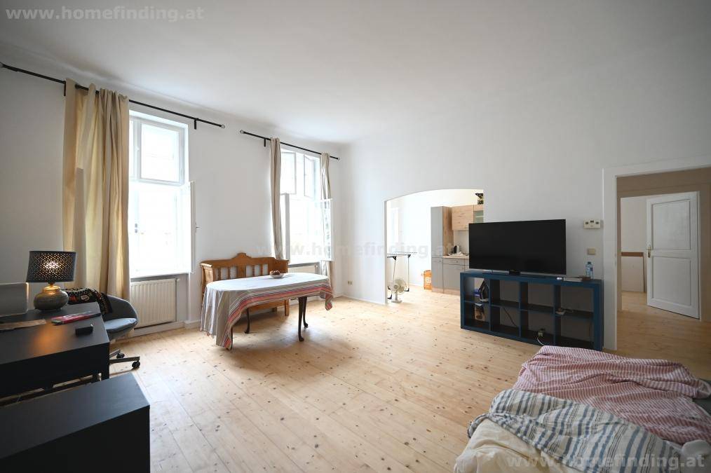 Geräumiger Wohn- und Essbereich mit hellem Holzfußboden, großen Fenstern und offenem Zugang zur Küche.