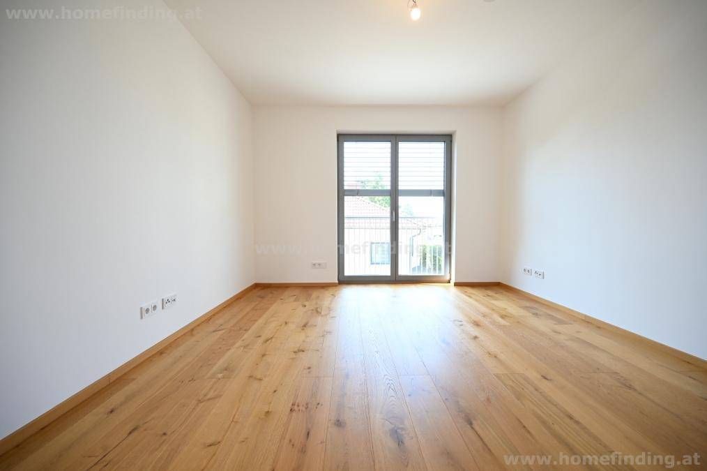 Helles Zimmer mit Holzboden und großer Fenstertür, die zu einem französischen Balkon führt.