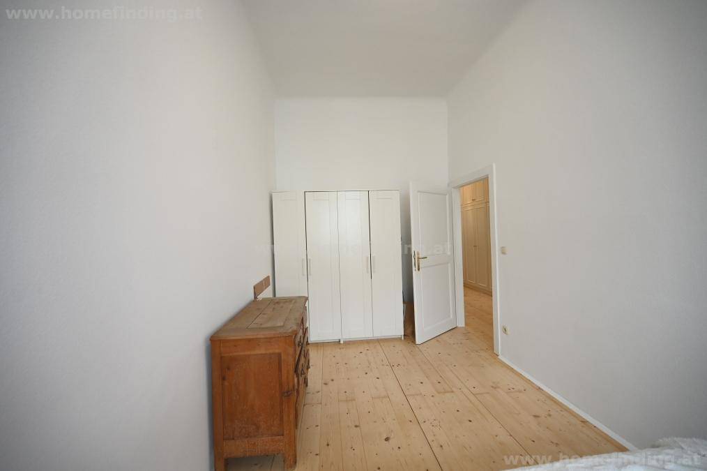 Schlafzimmer mit weißem Kleiderschrank, antiker Kommode und hellem Holzfußboden.