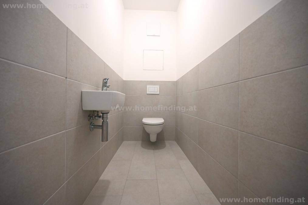 Separates Gäste-WC mit wandhängender Toilette und kleinem Waschbecken in neutralen Fliesen.