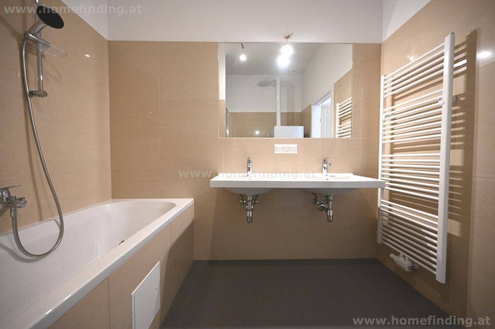 Modernes Badezimmer mit beigefarbenen Fliesen, Badewanne, Dusche und Doppelwaschbecken.