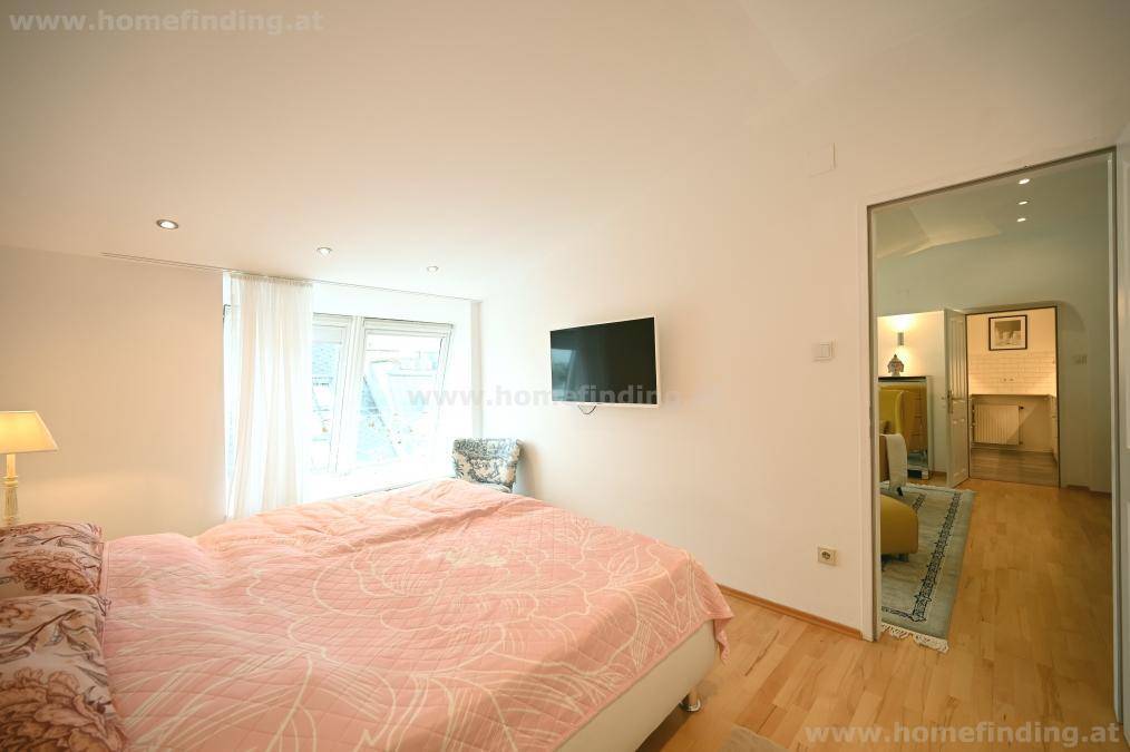 Helles Schlafzimmer mit Wandfernseher und Zugang zum Wohnbereich, ausgestattet mit Holzboden.