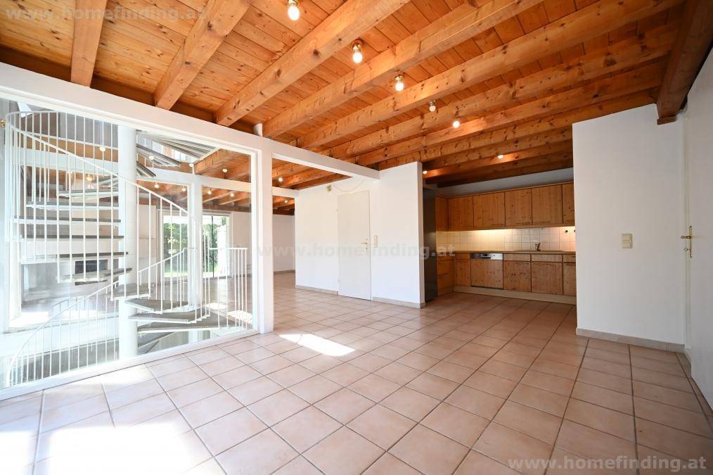 Offener Wohnbereich mit integrierter Küche, Fliesenboden und charakteristischen Holzdeckenbalken.