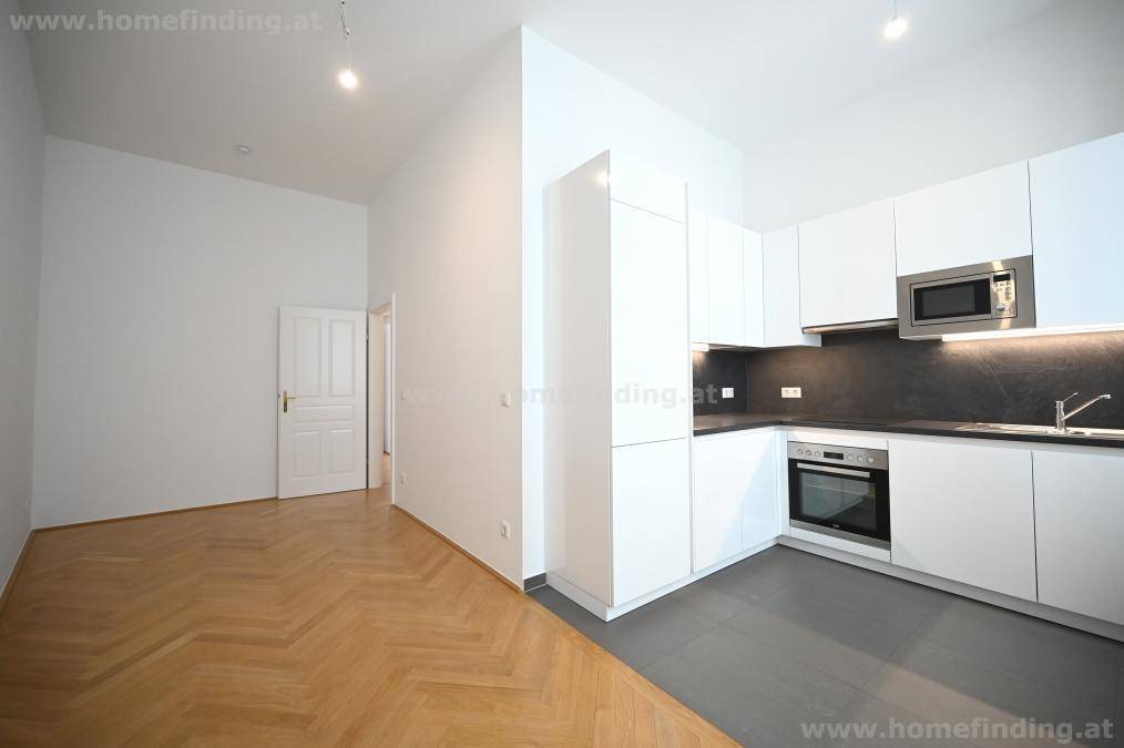 Offener Wohnbereich mit moderner Küche und angrenzendem Zimmer mit Fischgrätparkett.