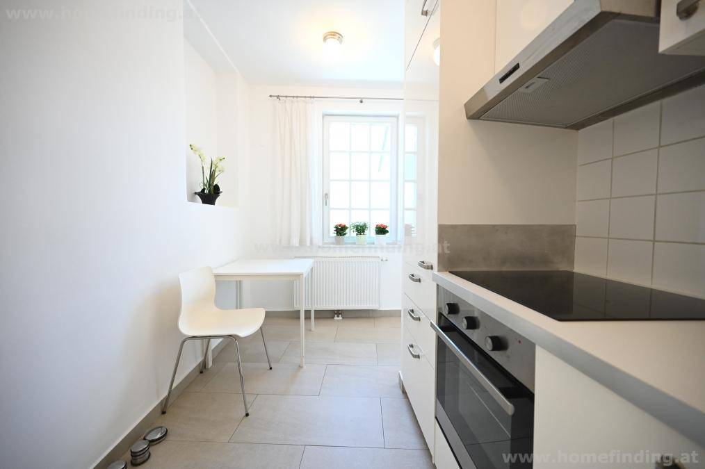 Funktionale Küchenzeile mit Kochfeld, Backofen, Spüle und kleinem Essbereich am Fenster.
