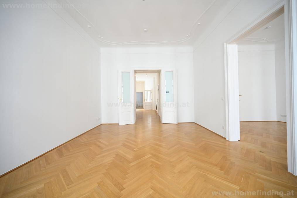 Elegantes Zimmer mit Fischgrätparkett und doppelten Flügeltüren, die zu weiteren Räumen führen.