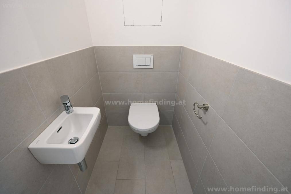 Funktionale Gästetoilette mit modernen hellgrauen Fliesen, wandhängendem WC und kleinem Handwaschbecken.