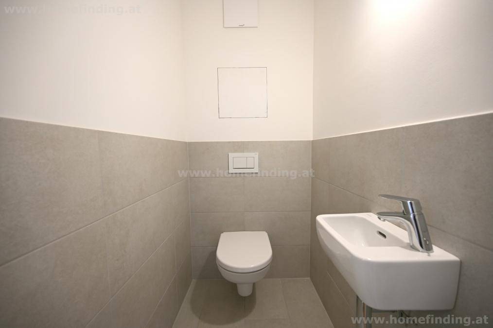 Separates Gäste-WC mit Wand-WC, kleinem Waschbecken und hellgrauen Wandfliesen.