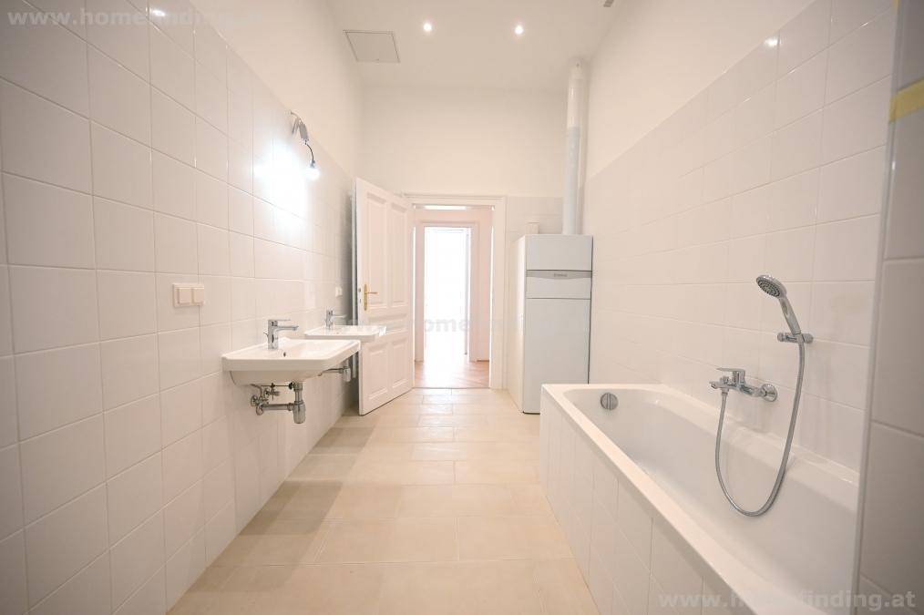 Großes, hell gefliestes Badezimmer mit zwei Waschbecken und einer Badewanne, in modernem Zustand.