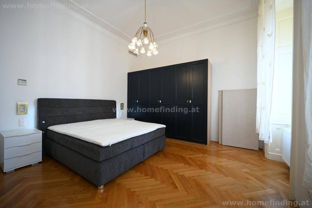 Geräumiges Schlafzimmer mit dunklem Bett, großem Kleiderschrank und klassischem Parkettboden für eine ruhige Atmosphäre.