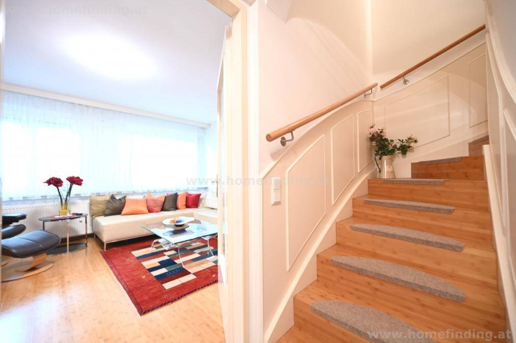 Holztreppe mit Geländer führt in die obere Etage, mit Blick auf das Wohnzimmer.