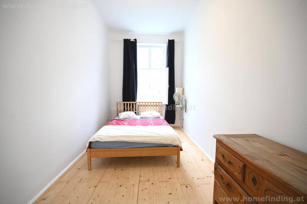 Gemütliches, schmales Schlafzimmer mit Einzelbett, Holzboden und einem Fenster mit dunklen Vorhängen.