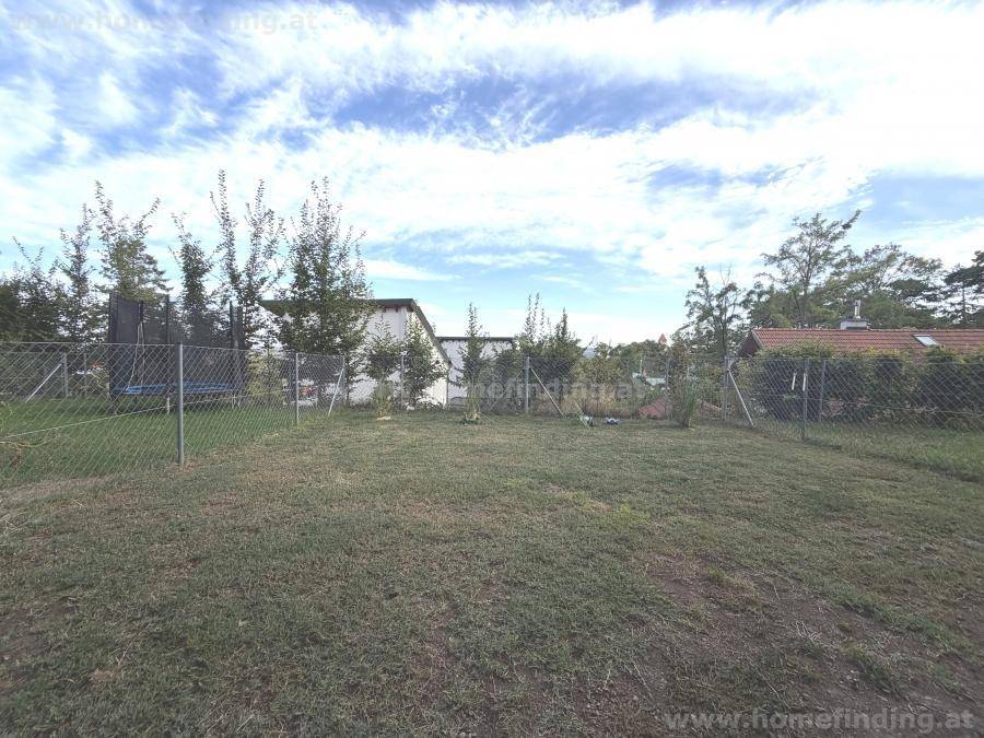Großer, gepflegter Gartenbereich mit Rasenfläche und Trampolin, umzäunt und von Bäumen umgeben.