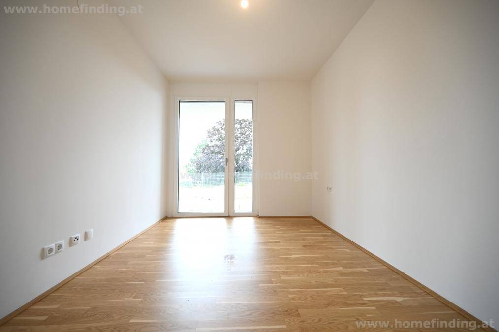 Helles Schlafzimmer mit Parkettboden und Zugang zu einem Außenbereich durch eine Glastür.