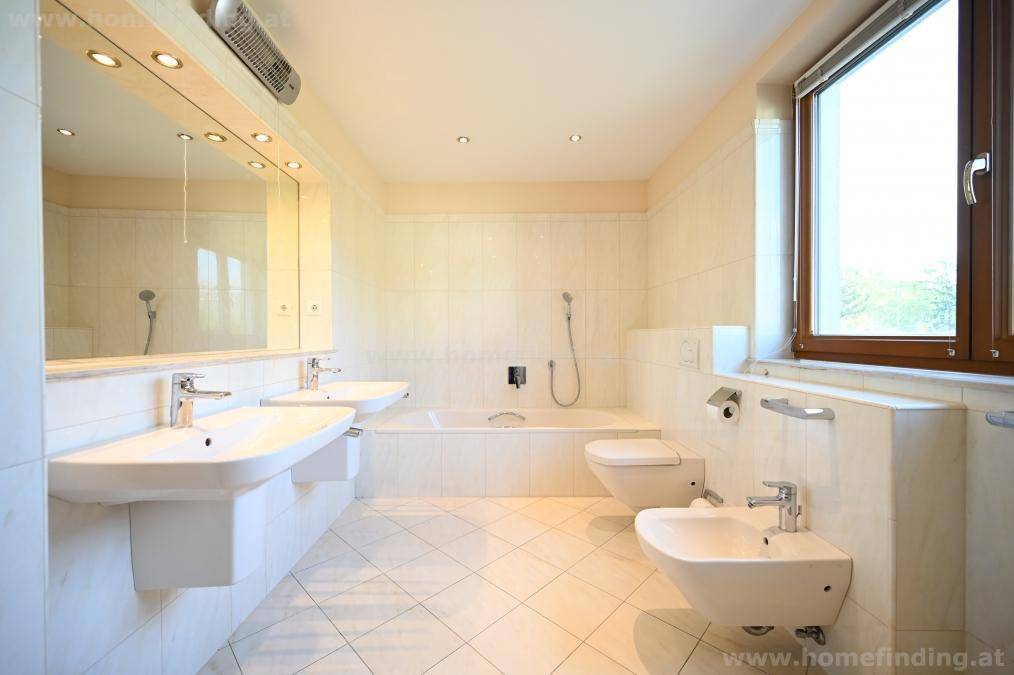 Geräumiges Badezimmer mit Doppelwaschbecken, Badewanne, Bidet und Fenster, ausgestattet mit hellen Fliesen.
