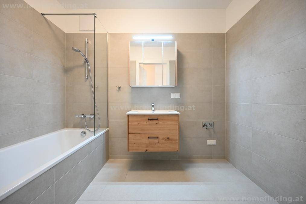 Modernes Badezimmer mit hellgrauen Fliesen, Badewanne mit Duschwand und schwebendem Holzwaschtisch mit Spiegelschrank.