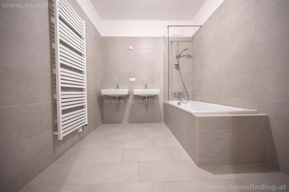Modernes Badezimmer mit doppelten Waschbecken, Badewanne mit Duschfunktion und Handtuchheizkörper.