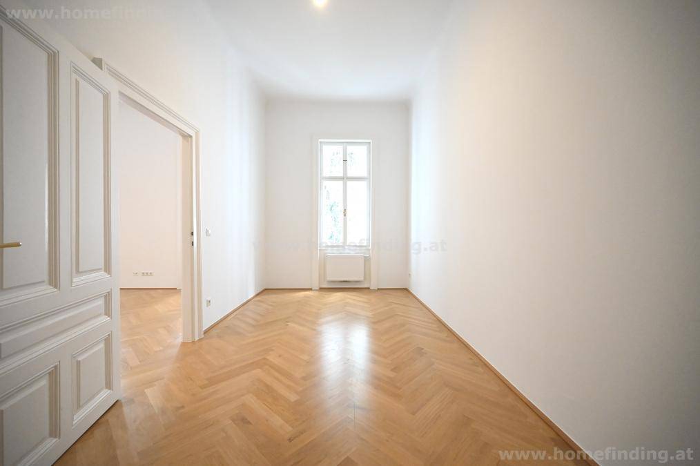 Langes, helles Zimmer mit Fischgrätparkett und einem hohen Fenster.