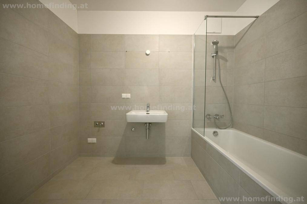 Modernes Badezimmer mit hellgrauen Fliesen, Badewanne mit Duschabtrennung und Waschbecken.