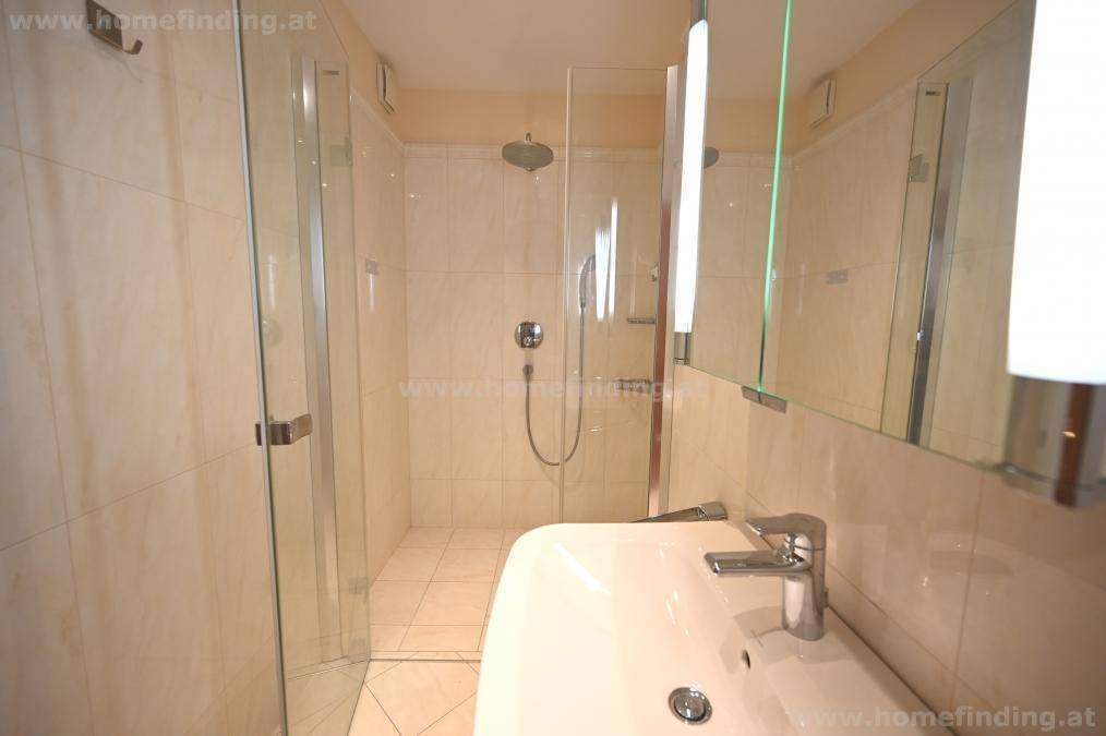 Modernes Badezimmer mit einer geräumigen begehbaren Dusche und einem einzelnen Waschbecken, hell gefliest.