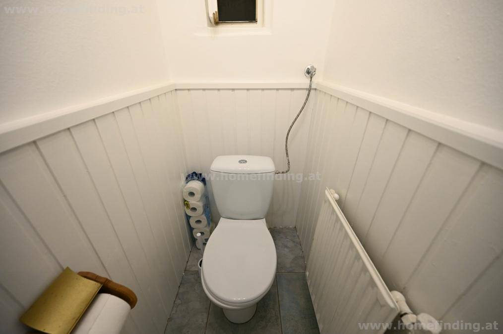 Separates WC mit Toilette, weißer Holzverkleidung und einem kleinen Fenster für Belüftung.