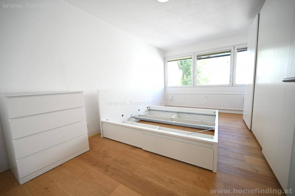Helles Schlafzimmer mit Holzboden, großen Fenstern und weißer Kommode, bereit zur individuellen Gestaltung.