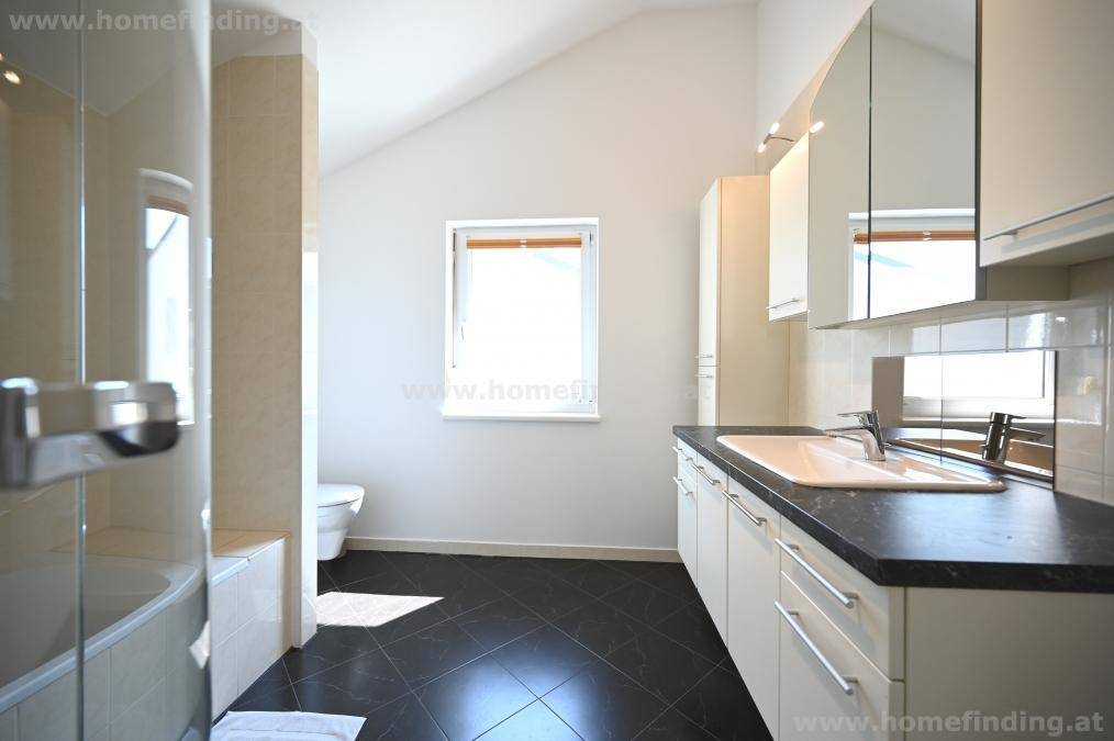 Modernes Badezimmer mit dunklen Fliesen, Waschtisch, Spiegelschränken und Dachschräge.