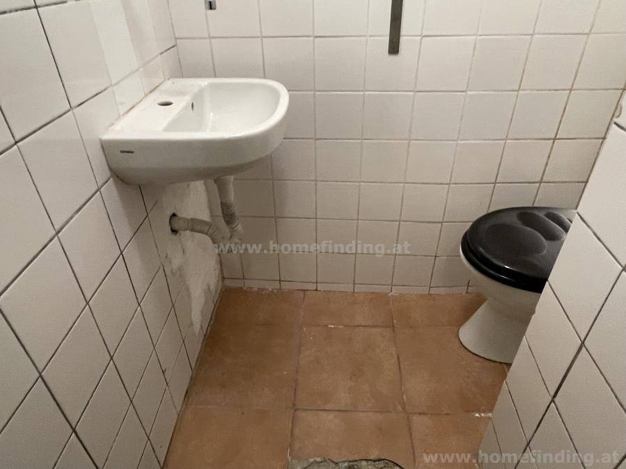 Einfacher Toilettenraum mit Waschbecken, WC und weiß gefliesten Wänden, zweckmäßig gestaltet.