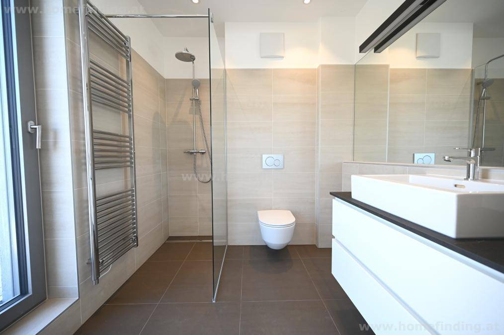 Elegantes Badezimmer mit ebenerdiger Dusche, Wand-WC und modernem Waschtisch, hell gefliest.
