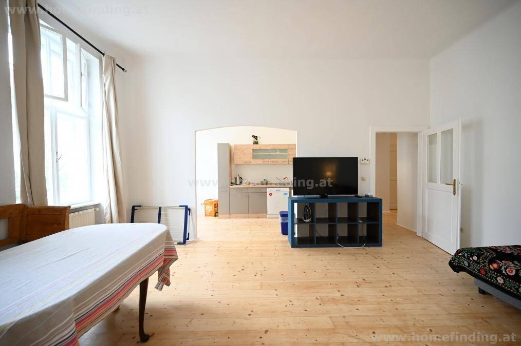 Geräumiger Wohn-Essbereich mit Holzboden und offenem Zugang zur Küche durch einen eleganten Bogen.
