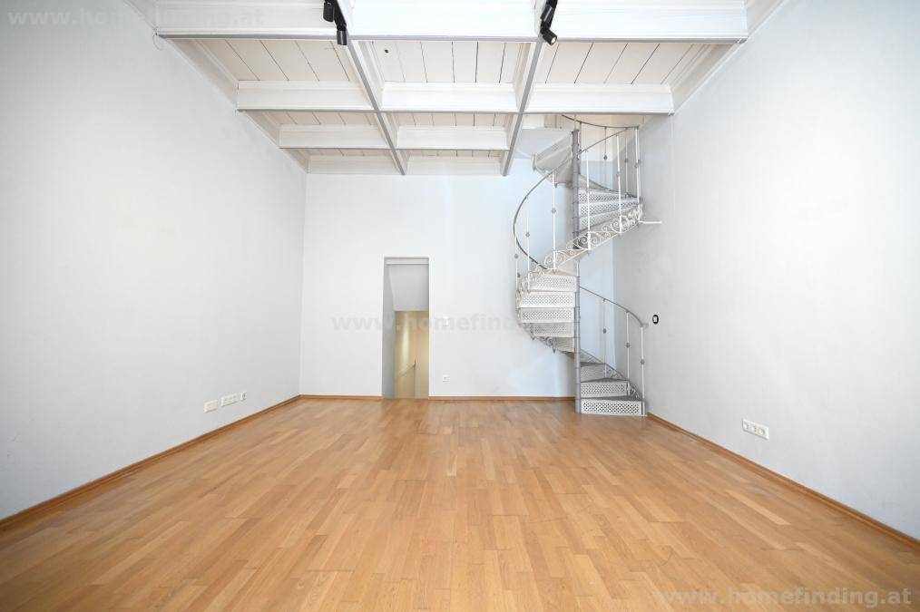 Geräumiges Zimmer mit Holzboden, sichtbaren Deckenbalken und einer eleganten Wendeltreppe.