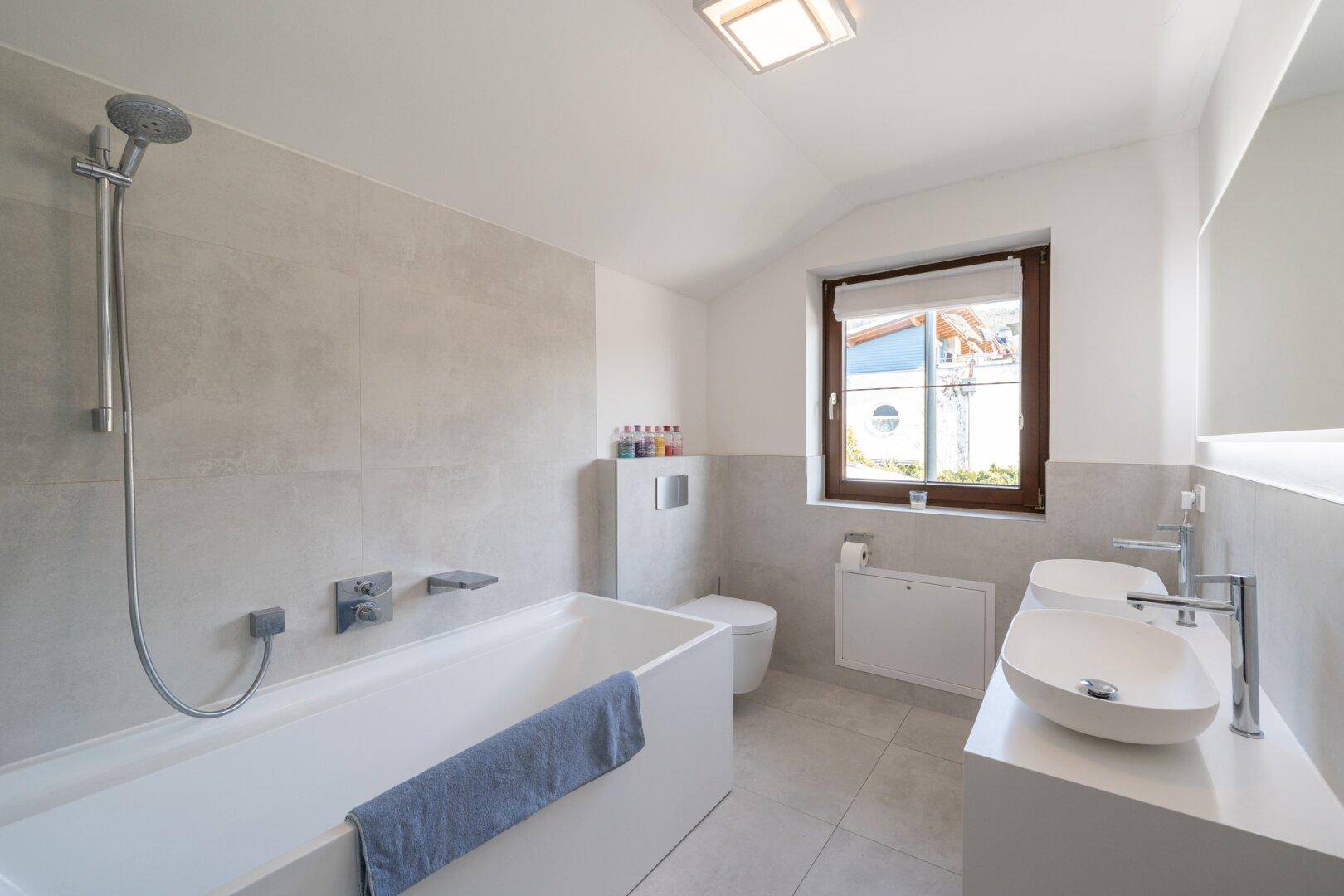 Modernes Badezimmer mit Badewanne, Doppelwaschbecken und Fenster für Tageslicht.