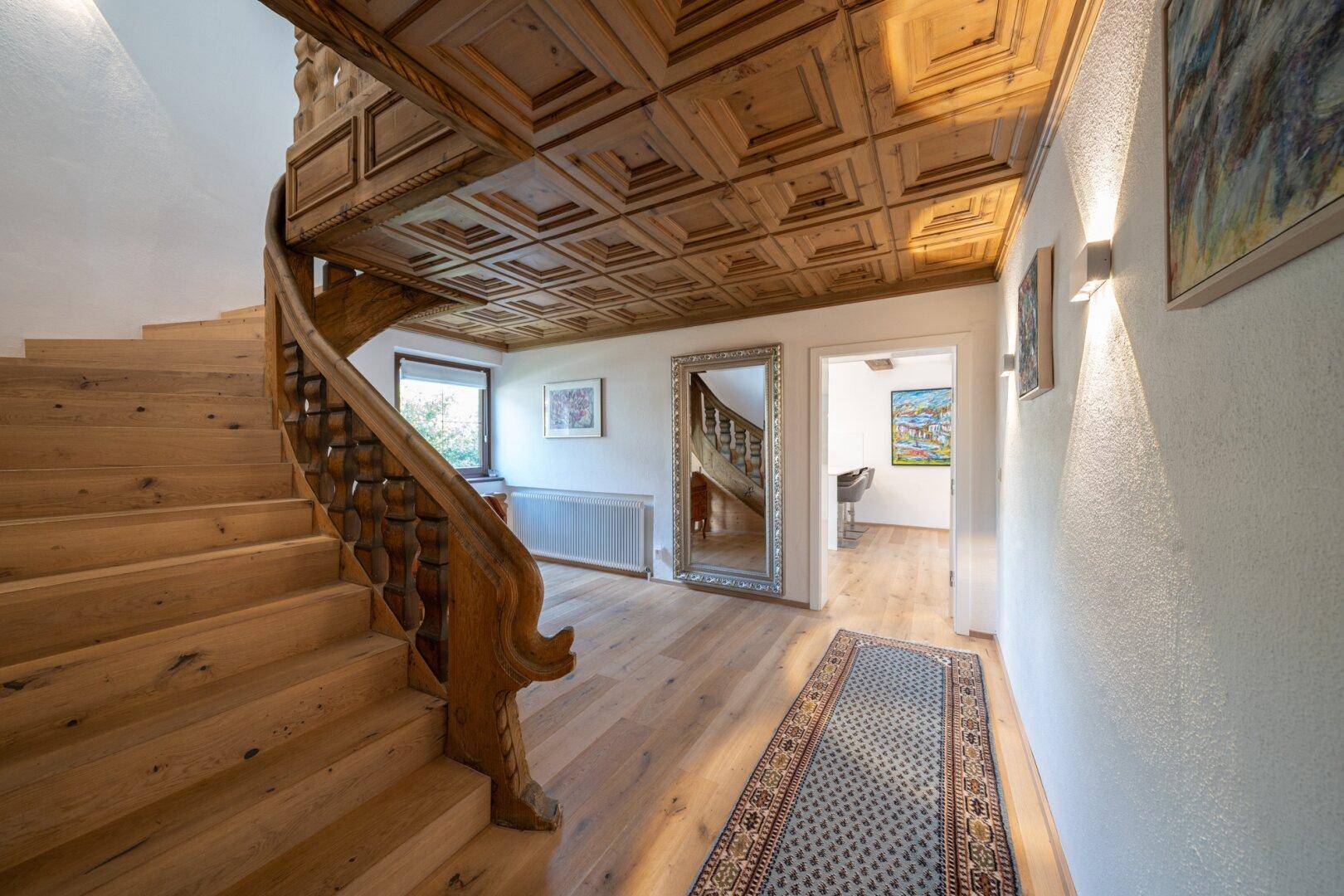 Eindrucksvoller Treppenaufgang mit geschnitztem Holzgeländer und Kassettendecke aus Holz.