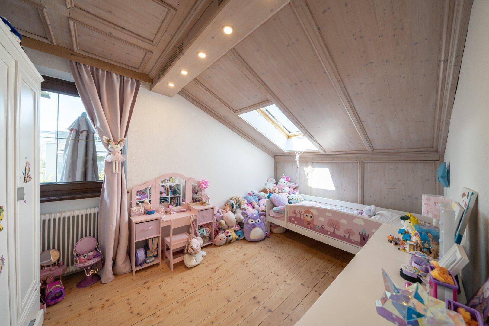 Kinderzimmer im Dachgeschoss mit Holzbalkendecke, Dachfenster und Spielzeug.