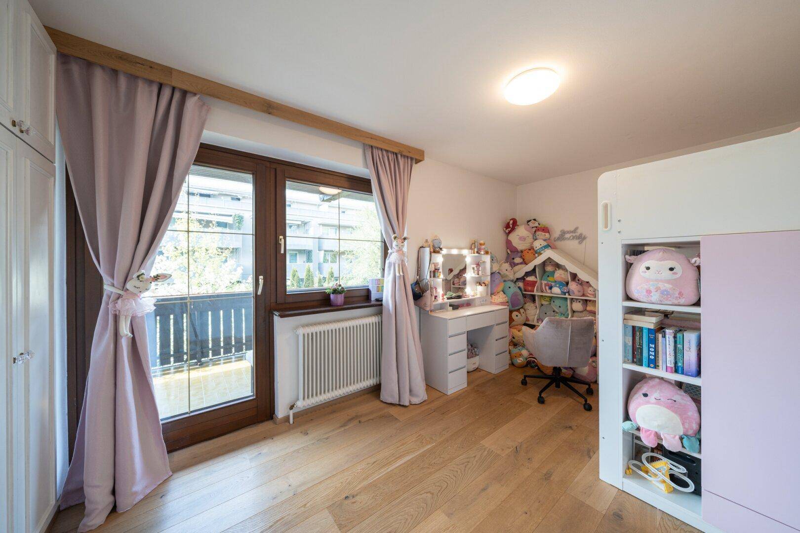Helles Kinderzimmer mit Balkonzugang, Holzboden und Schminktisch.