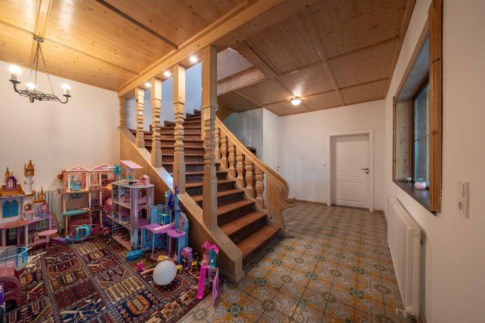 Rustikaler Eingangsbereich mit Holztreppe, Holzbalkendecke und farbigen Fliesen.