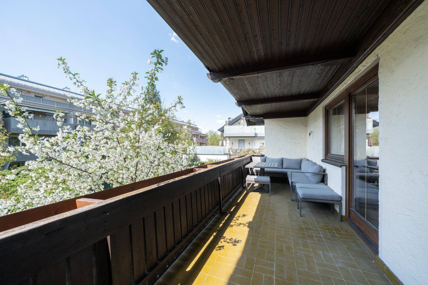 Großer Balkon mit Sitzgelegenheiten und Blick auf blühende Bäume und die Umgebung.