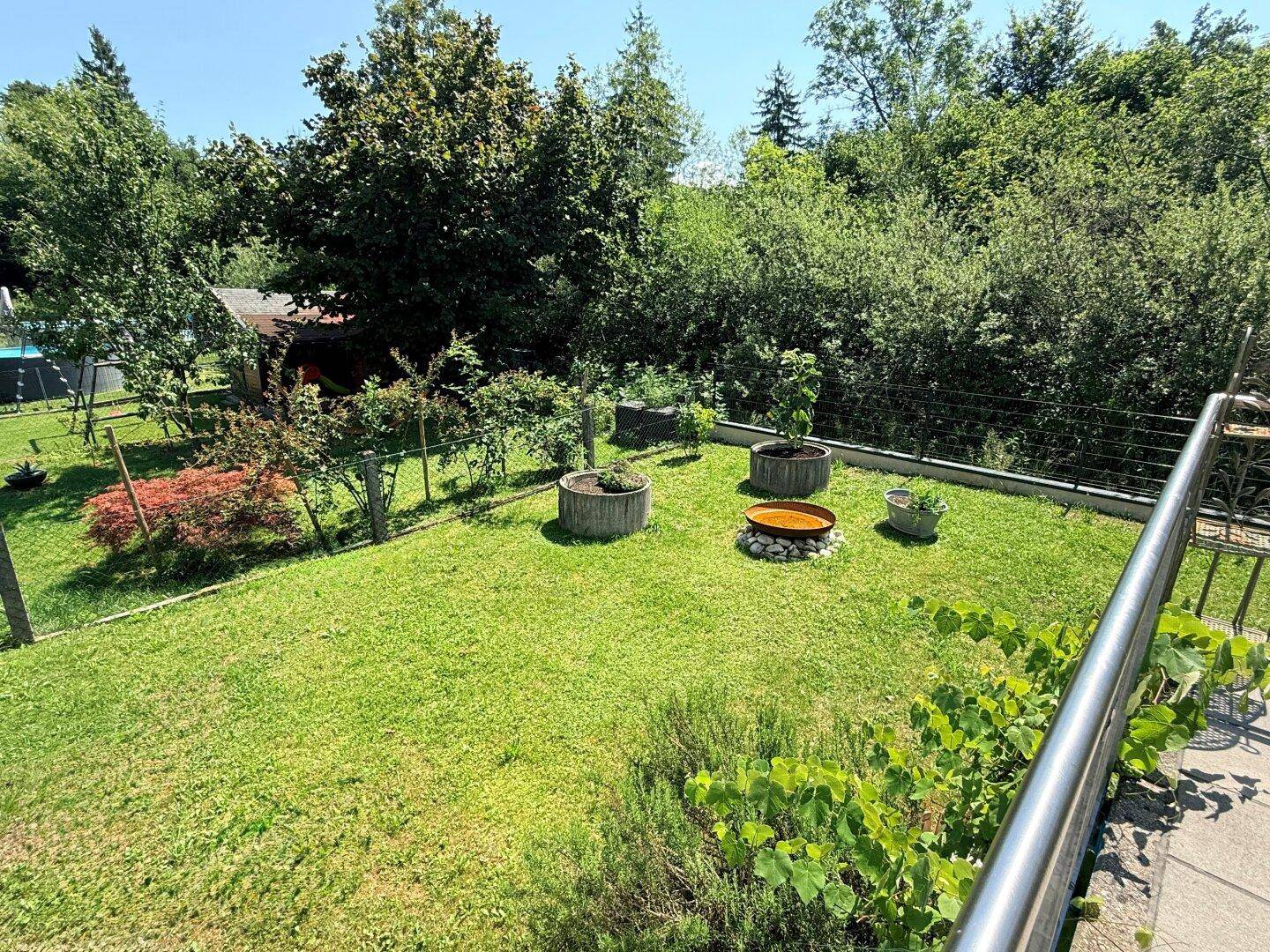 Gepflegter Gartenbereich mit Rasenfläche, kleinen Bäumen und einer Feuerstelle.
