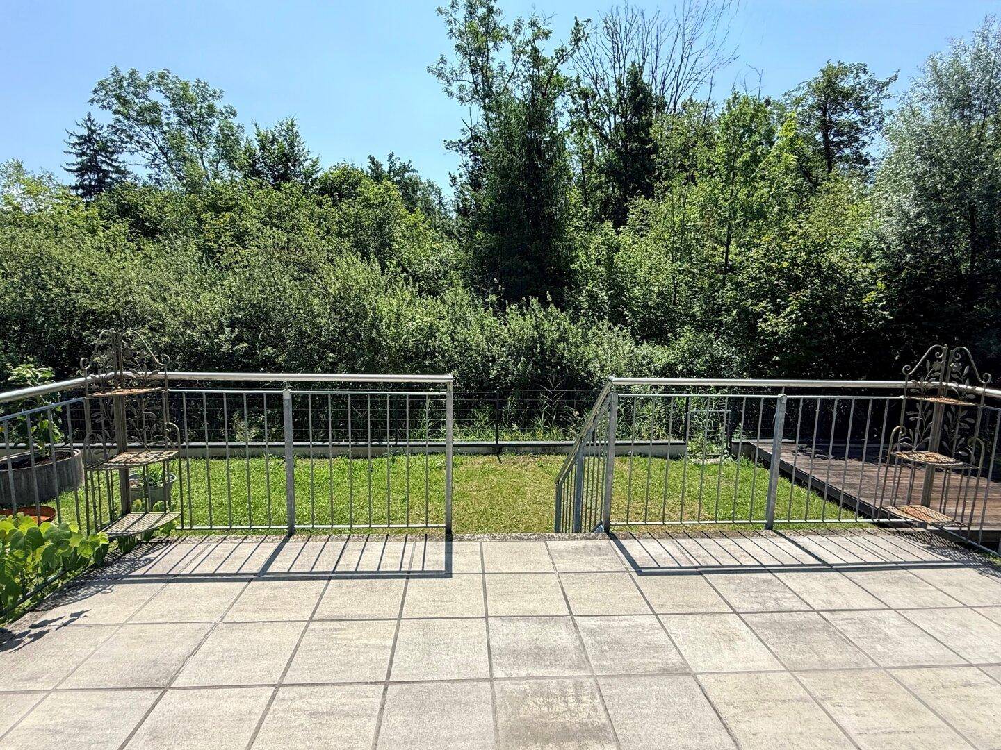 Geräumige Terrasse mit Fliesenboden und Treppenzugang zum grünen Gartenbereich.