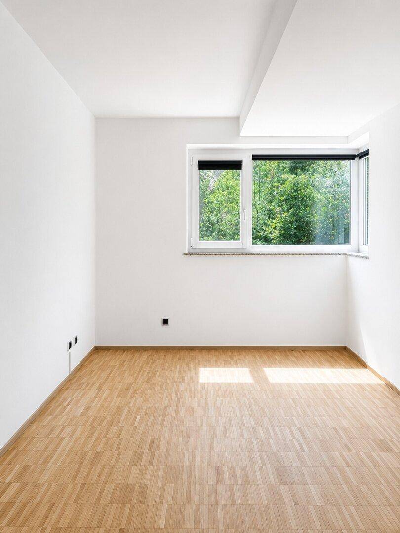 Helles Zimmer mit Parkettboden und großem Fenster mit Blick ins Grüne.